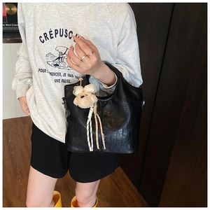 Detail of black crocodile texture handbag featuring a cute plush bear pendant accessory