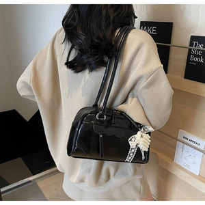 Detail of black glossy Boston bag with pearl bow charm and elegant wave pleated texture