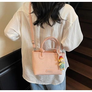 Pink woven bucket bag with adjustable strap and cute cartoon doll pendant on model