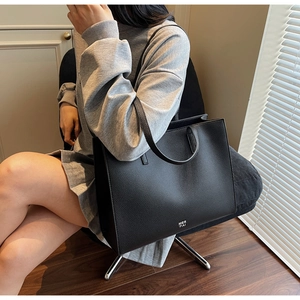 Detail showing high-quality black litchi pattern leather and white logo on tote bag