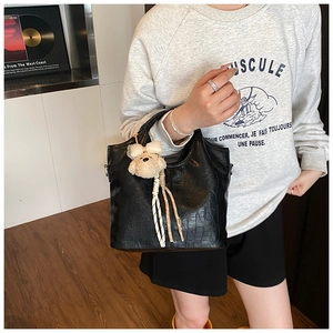 Detail of black crocodile pattern bucket bag with a cute plush bear charm on model