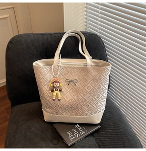 Detail of off-white tote bag with floral embroidery, silver bow, and pearl doll charm