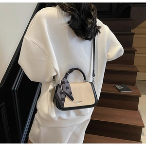 Chic beige fabric and black leather crossbody bag styled on a wooden staircase