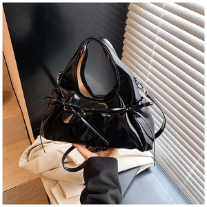 Detail of black patent leather bag featuring glossy finish and elegant ribbon bow detail