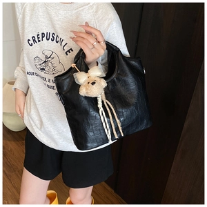 Detail of black crocodile texture handbag featuring a cute plush bear charm accessory
