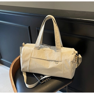 Detail view of beige nylon travel bag with dual handles and shoulder strap on a chair
