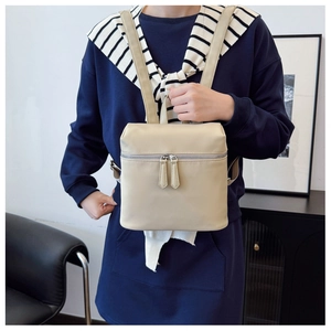 Close-up of lightweight beige faux leather backpack styled on model with navy sweatshirt