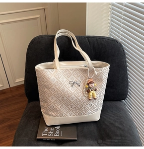 Detail shot of white geometric pattern tote bag with silver bow and cartoon doll charm