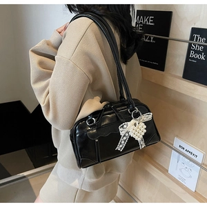 Detail of black leather shoulder bag with white lace bow and pearl heart charm accessory
