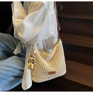 Detail of cream woven shoulder bag with hollow mesh design and cute cartoon pendant