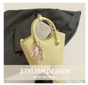 Detail of yellow bucket bag featuring pearl heart charm and pink ribbon on handle