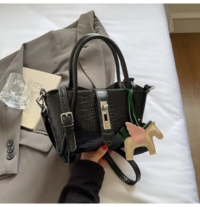 Detail of black crocodile texture handbag with horse charm on elegant grey fabric