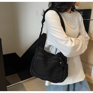 Detail of black canvas crossbody bag with multiple zippers and wide shoulder strap
