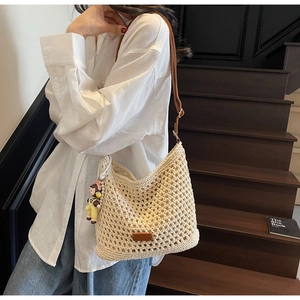 Detail of hand-woven cream tote bag with brown leather strap and cute doll pendant accessory