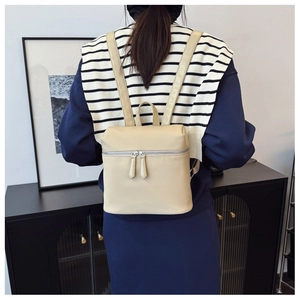 Detailed back view of a beige minimalist backpack with metal zippers and adjustable straps