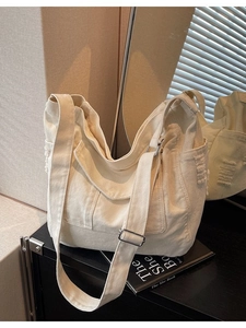 Large cream canvas tote bag with adjustable strap and frayed side pocket on metal cabinet