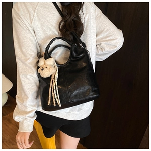 Detail view of black glossy crocodile textured handbag with a cute plush bear pendant