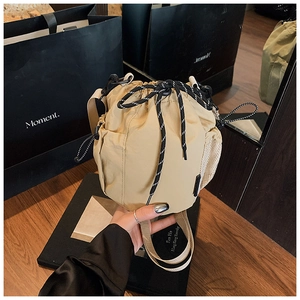 Detail of beige nylon drawstring bucket bag with mesh side pocket and thick cord strap