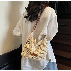 Detail of hollow woven tote bag with brown leather straps and cute girl charm