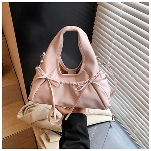 Detail shot of a pink pleated crossbody bag featuring decorative bows and metal connectors