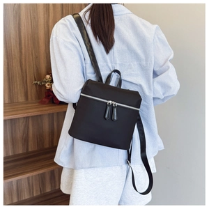 Rear view of a minimalist black nylon backpack worn on back over a striped shirt