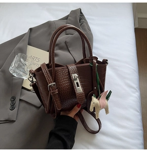 Detail of dark brown crocodile embossed handbag with pony charm and silver hardware