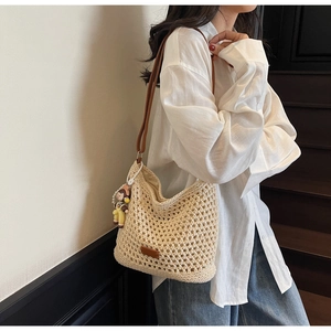Macro shot of beige crochet hollow tote bag featuring a brown leather strap and doll pendant