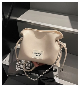 Detail of cream drawstring bucket bag with mikaxiqi leather patch and chain strap