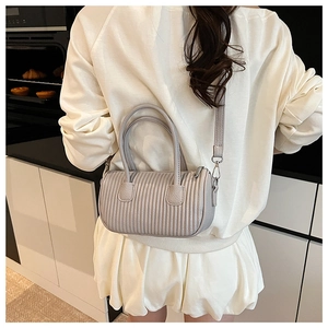 Detail of light grey pleated cylinder bag with silver metal hardware and crossbody strap