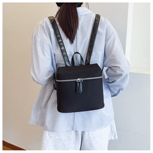 Black nylon backpack featuring double zippers and leather straps on model in simple interior