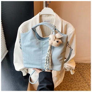 Detail of light blue faux crocodile bucket bag with plush bear charm and chain strap