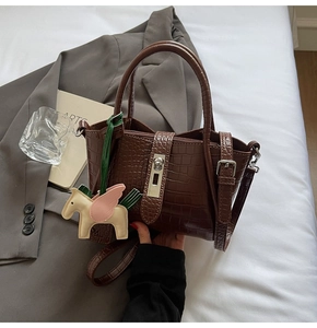 Detailed close-up of dark brown crocodile pattern handbag with elegant horse pendant decor