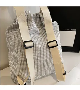 Detail of plaid drawstring backpack with adjustable wide cream straps on a stone surface