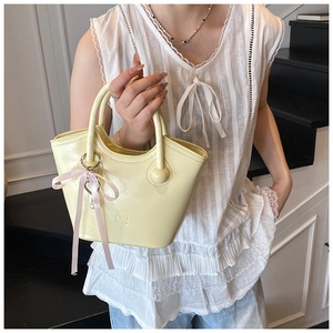 Détail d'un sac cabas jaune pâle avec nœud en soie rose et pendentif en perles