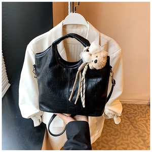Close-up of black crocodile pattern leather handbag with adjustable strap and cute bear charm
