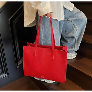 Detail of red pebbled leather tote bag with golden logo on deep wood background