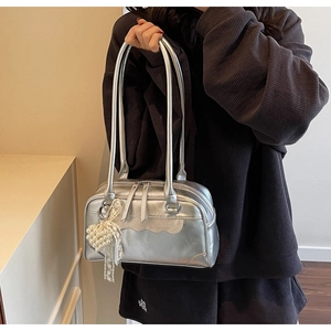 Close-up of metallic silver shoulder bag featuring dual zippers and pearl heart pendant