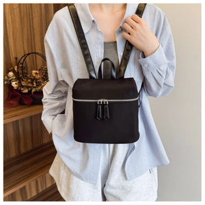 Detail shot of a black nylon mini backpack featuring silver zippers and leather pulls