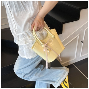 Détail d'un mini sac à main crème avec un nœud rose et un pendentif perle