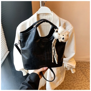 Detail view of black crocodile pattern tote bag with cute plush bear charm on white suit
