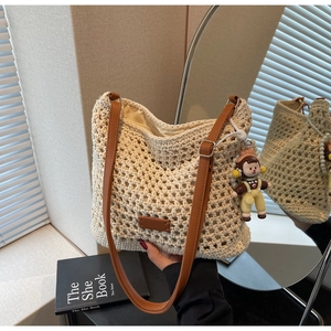 Close-up of cream woven tote bag with brown leather straps and a small cartoon doll pendant