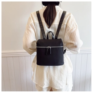 Detail of a black mini nylon backpack with silver zippers worn over a striped shirt