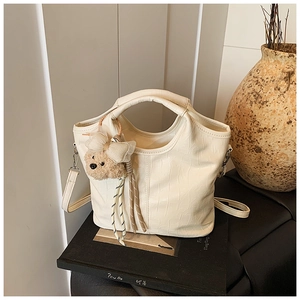 Detail of cream crocodile embossed handbag featuring a cute plush bear charm accessory
