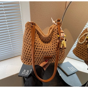 Detail view of woven straw bag with hollow pattern, leather strap and cute doll charm