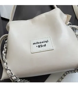 Detail of off-white PU leather shell bag featuring rectangular logo tag and silver chain strap