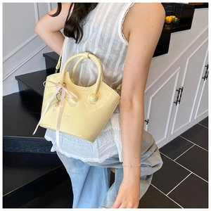 Detail of yellow glossy bucket bag with silk bow and pearl charm on white lace top