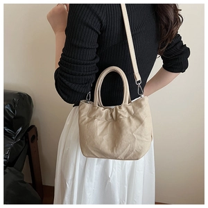 Detailed side view of a pleated beige handbag with a slim strap on a female model