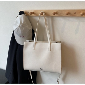 Close-up of cream lychee-textured leather tote bag hanging on a wooden coat rack