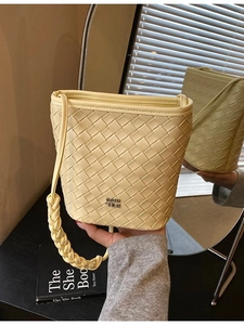 Pale yellow woven bucket bag with unique braided handle and metallic logo in a mirror setting