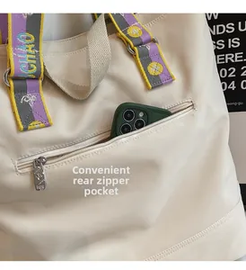Detail of a beige canvas tote bag showing a functional rear zipper pocket for a smartphone